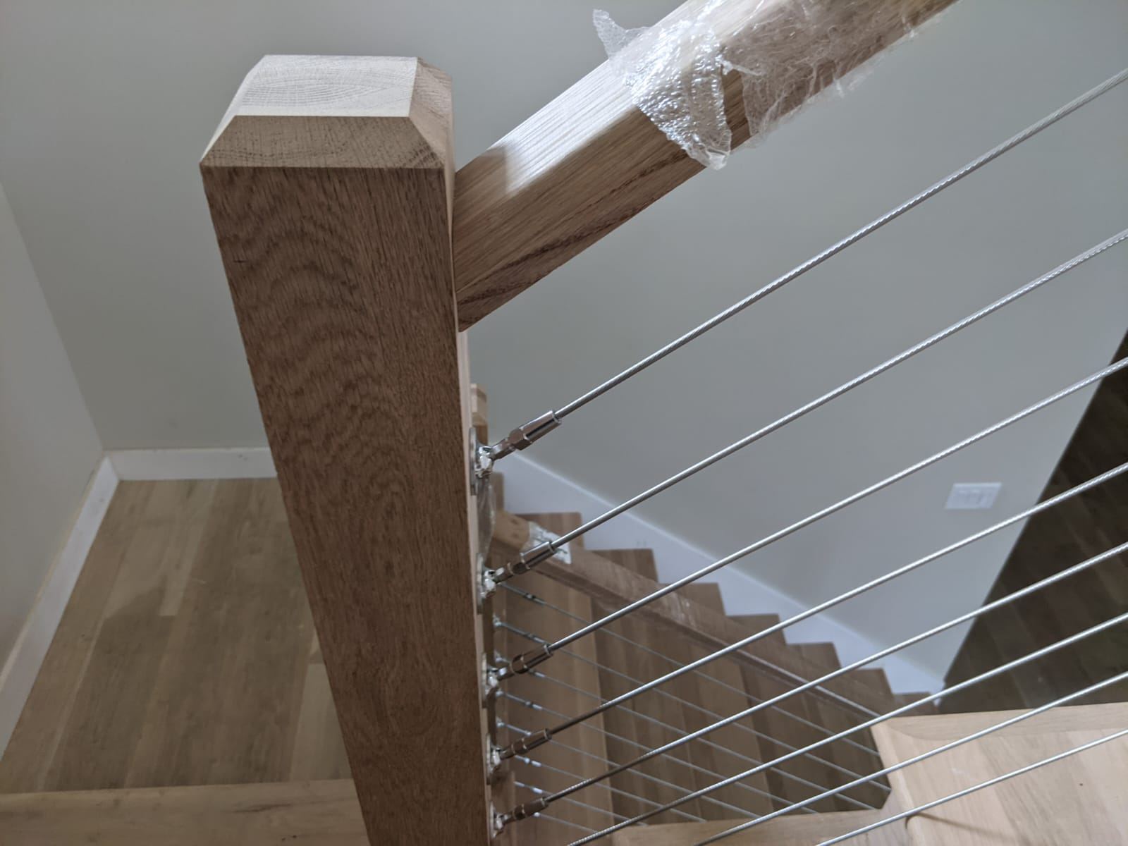Close detail of a stainless cable rail post fitted into a white oak newel